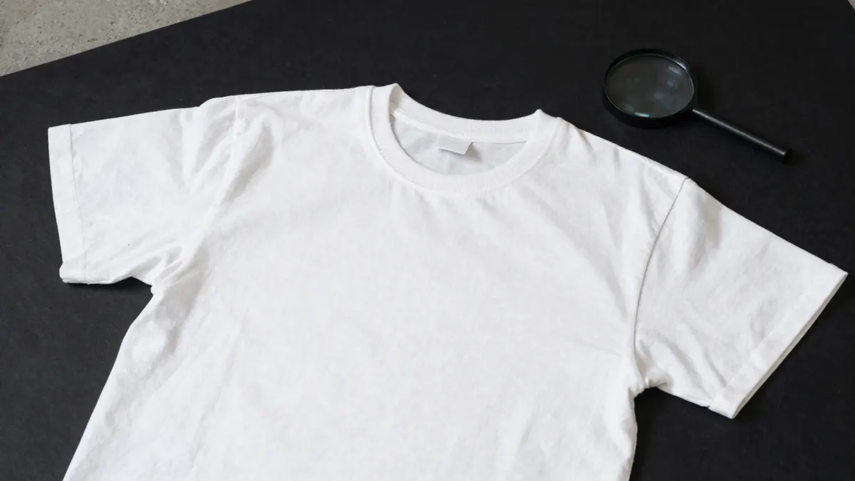 Plain white cotton tee with ribbed collar and faded fabric laid on dark cloth, checking a second-hand Stussy basic tee