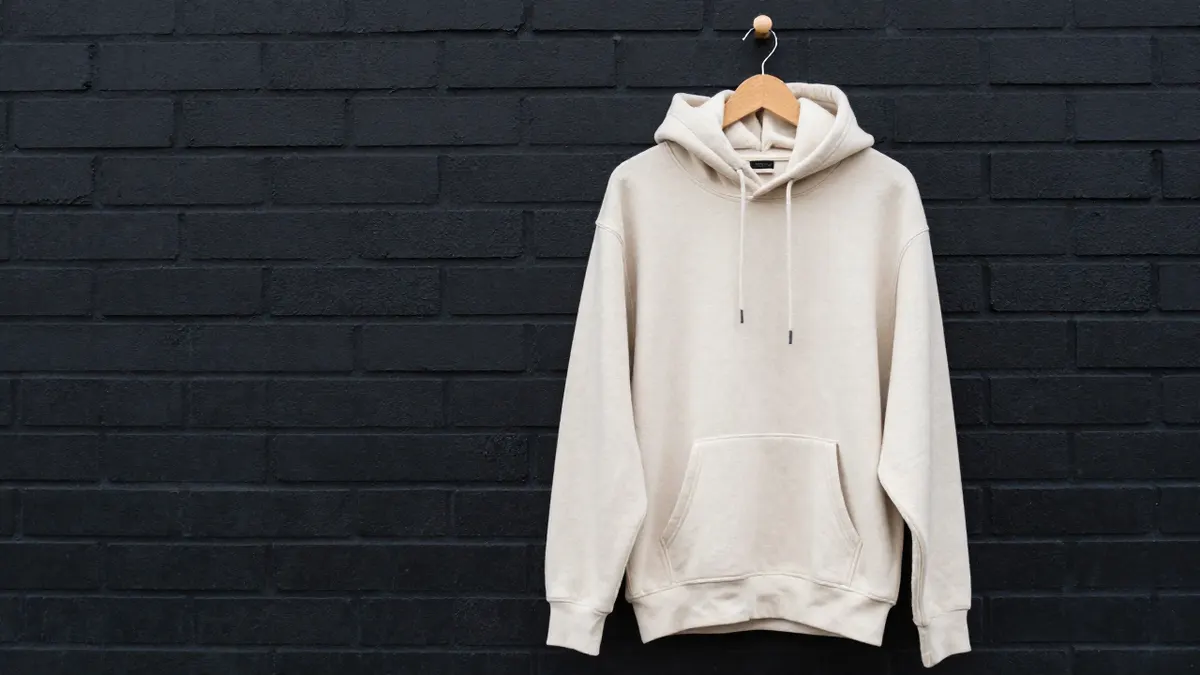 Cream fleece hoodie with relaxed fit and front pocket hanging on a wooden hook, illustrating a Stussy hoodie buying guide